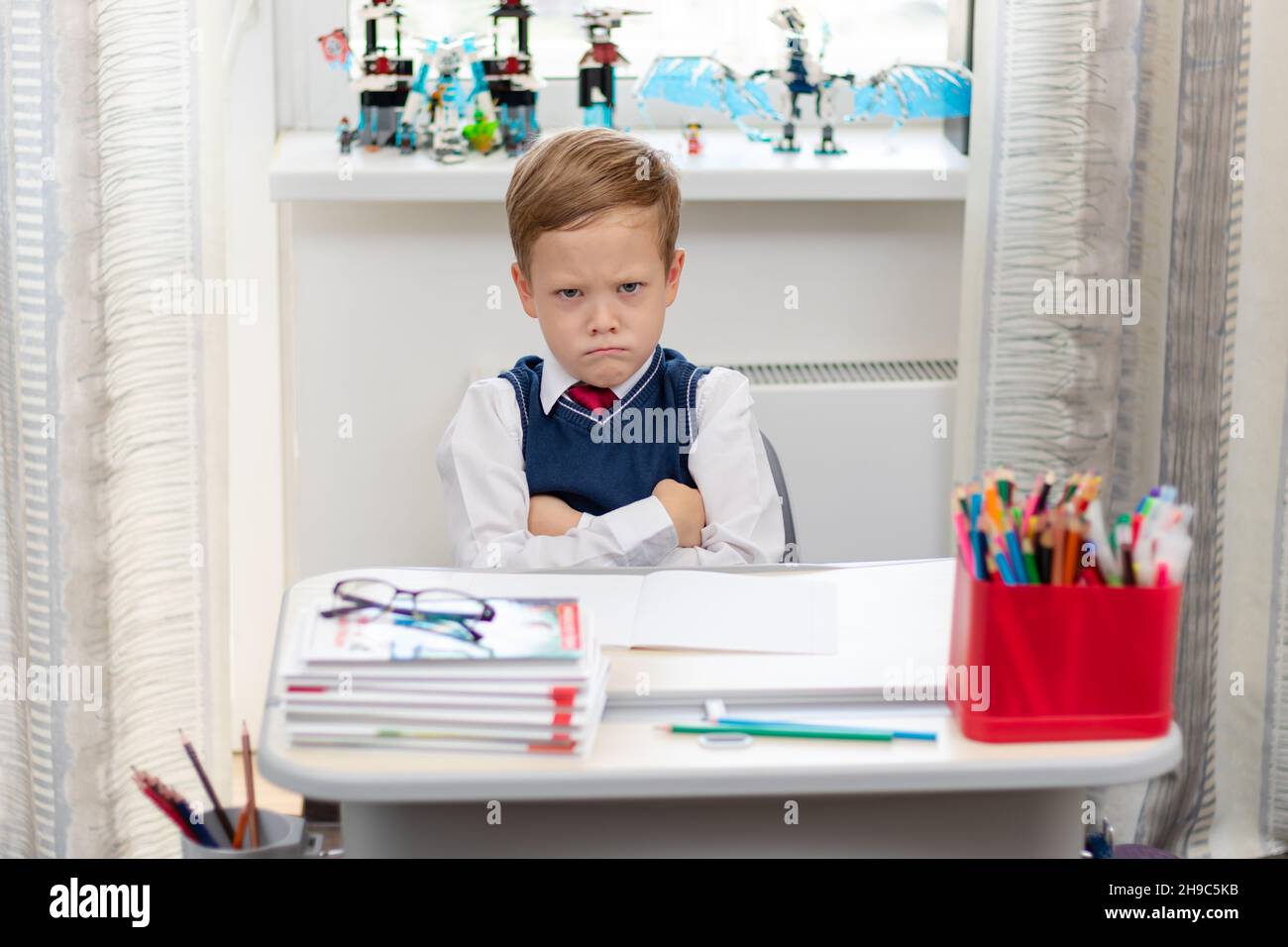 Carino ragazzo prima livellatore in uniforme scuola a casa durante una pausa folgorante mentre si siede alla sua scrivania. Messa a fuoco selettiva. Primo piano. Verticale Foto Stock