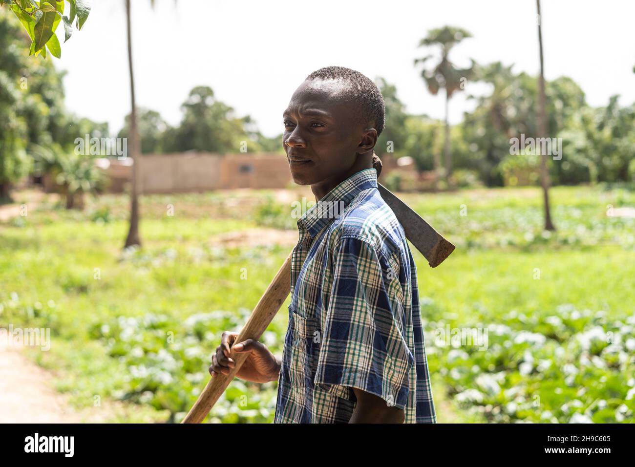 Il giovane agricoltore africano, premuroso e nero, con una zappa sulla spalla che fissava l'orizzonte Foto Stock