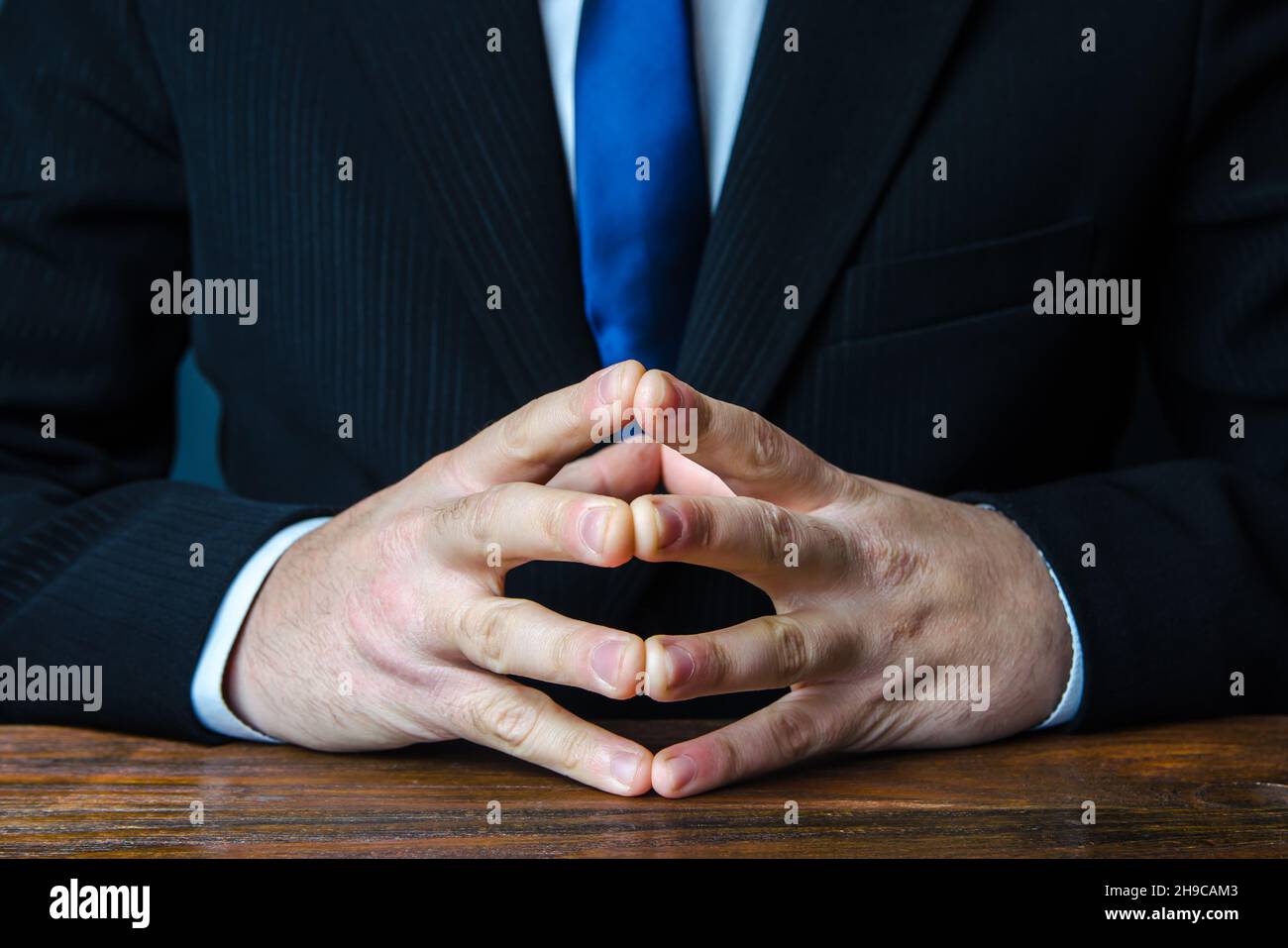 Un uomo siede con le mani in blocco. Gesto di consolidamento e deliberazione della forza. Tranquillità e calcolo a freddo. Risoluzione dei conflitti, ricerca Foto Stock