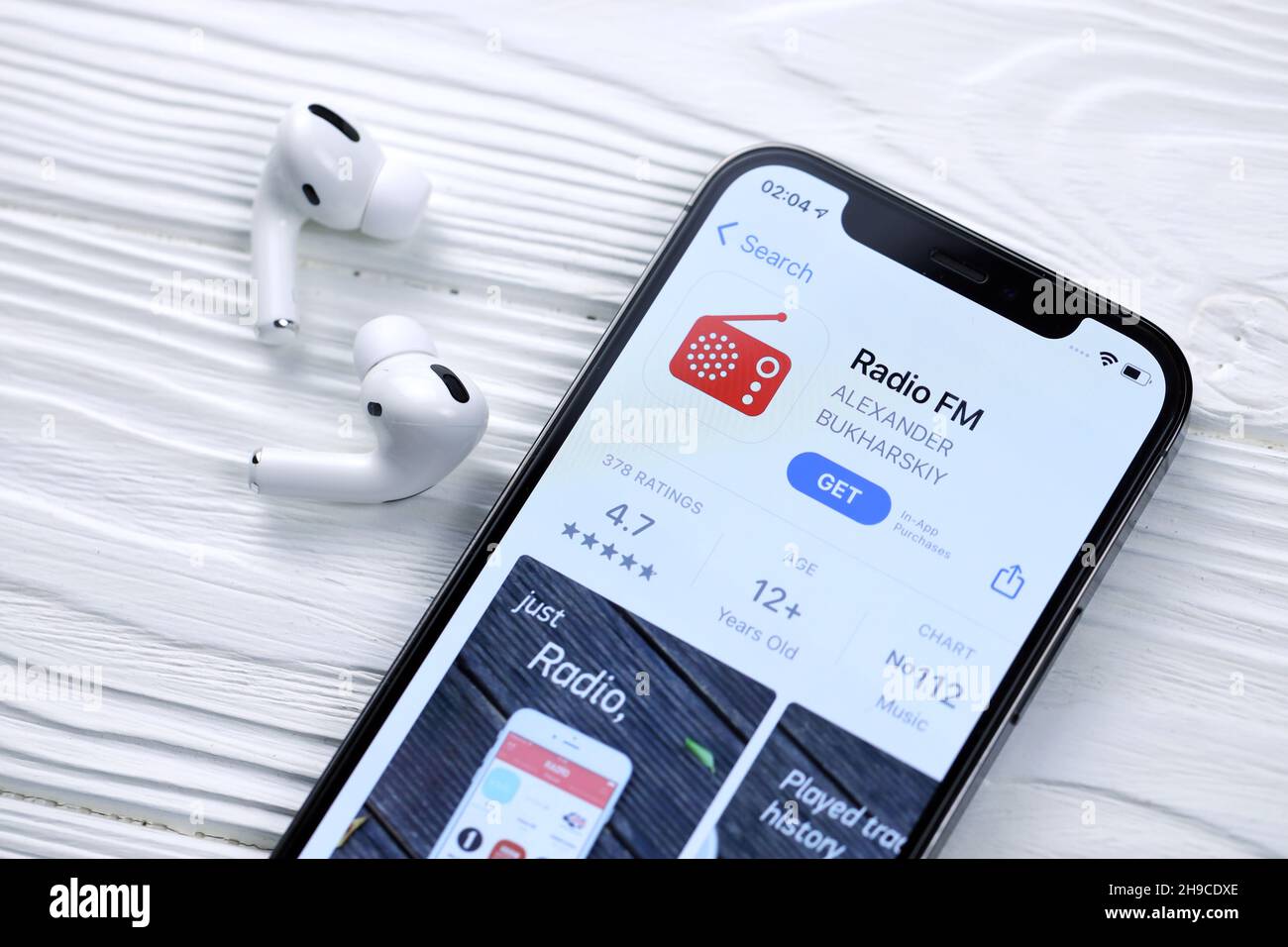 KHARKOV, UCRAINA - 5 MARZO 2021: Radio fm icona e applicazione da App Store su iPhone 12 schermo pro con airpods pro su tavolo bianco in legno Foto Stock