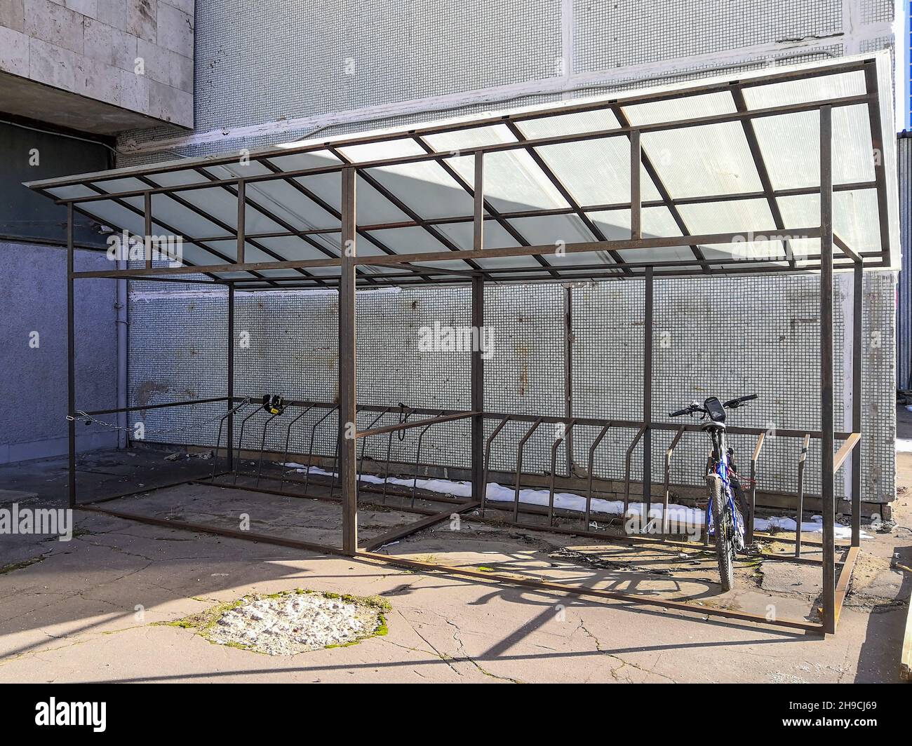 Una bicicletta lone si trova in un'area parcheggio coperto per biciclette vicino a un edificio grigio in cemento in una soleggiata giornata invernale. Paesaggio industriale. Foto Stock