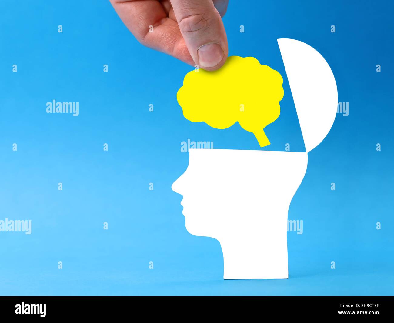 Mano che mette il cervello in testa aperta su sfondo blu, immagine concettuale del pensiero nuovo e creativo con spazio di copia Foto Stock