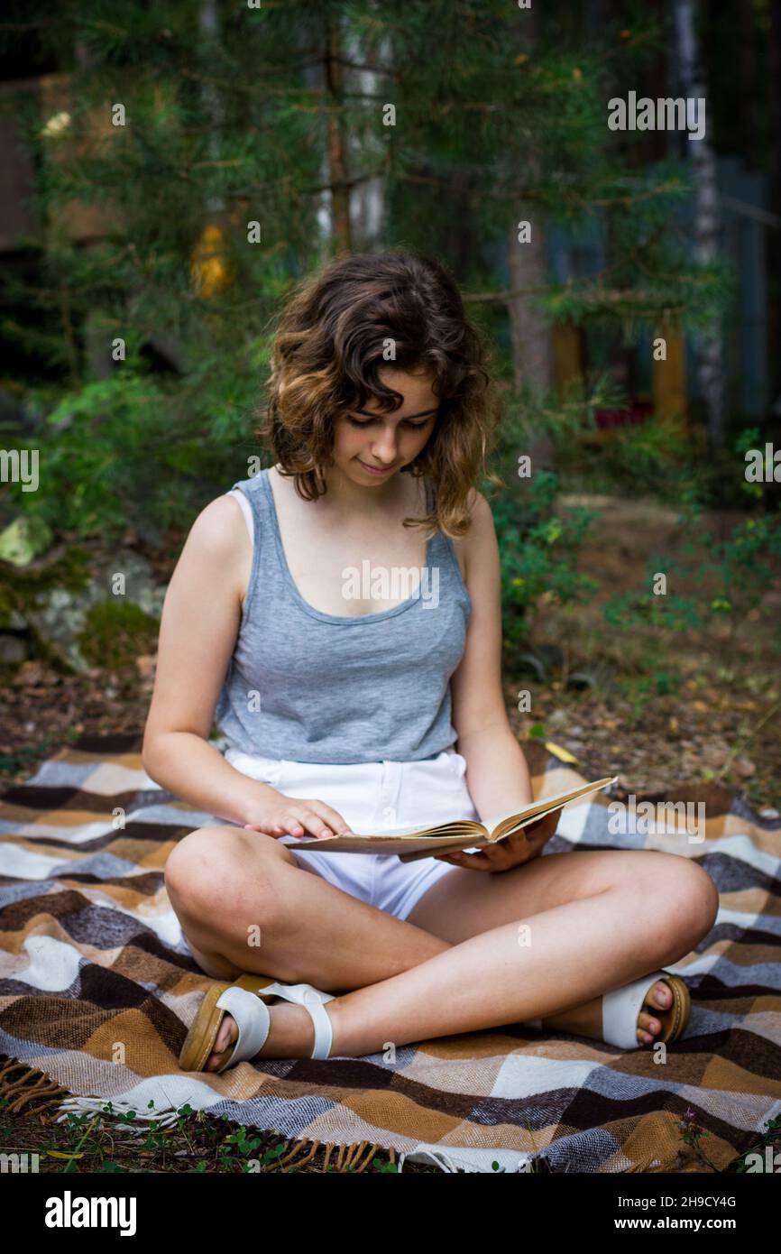Bella ragazza adolescente che legge un libro che giace su coperta su erba verde ai boschi. Foto Stock