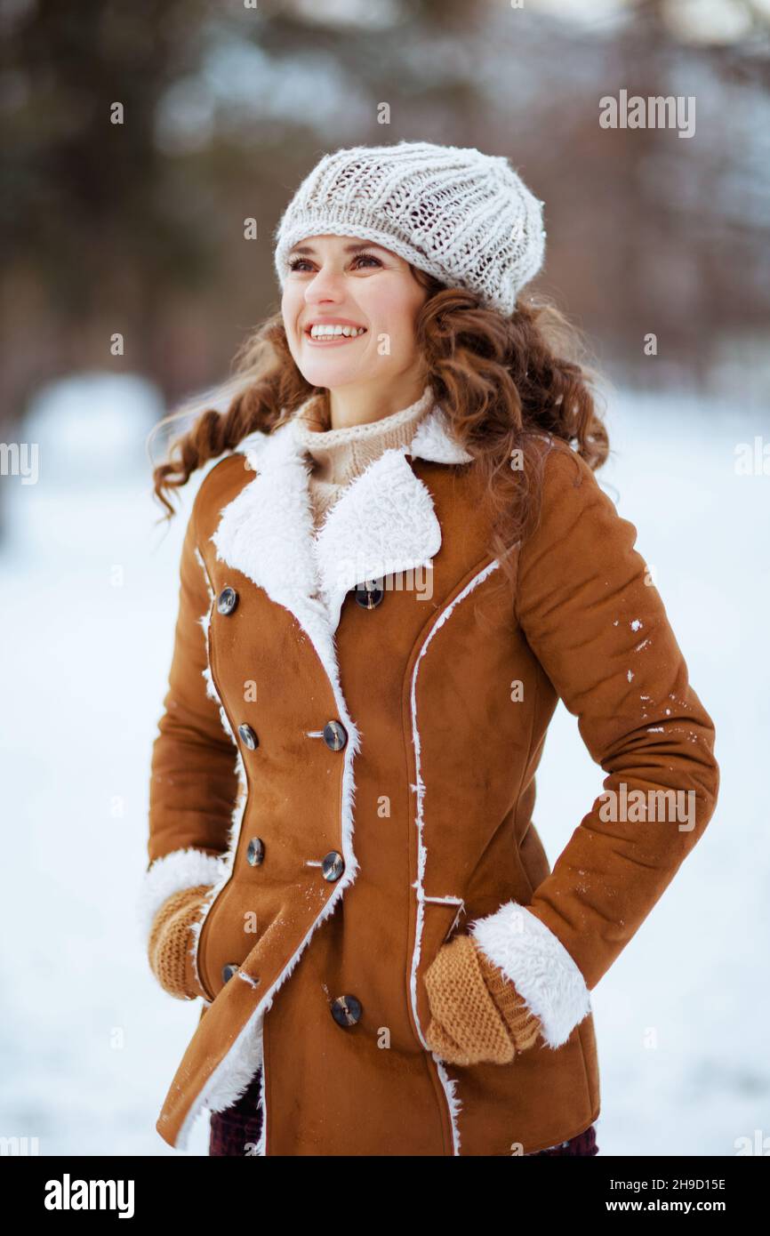 donna sorridente di 40 anni con guanti in maglia e cappotto in pelle di pecora all'aperto nel parco cittadino in inverno. Foto Stock