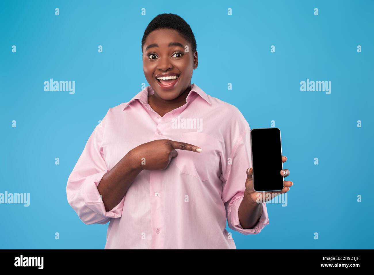 Donna nera che mostra lo schermo del telefono, puntando il dito su sfondo blu Foto Stock