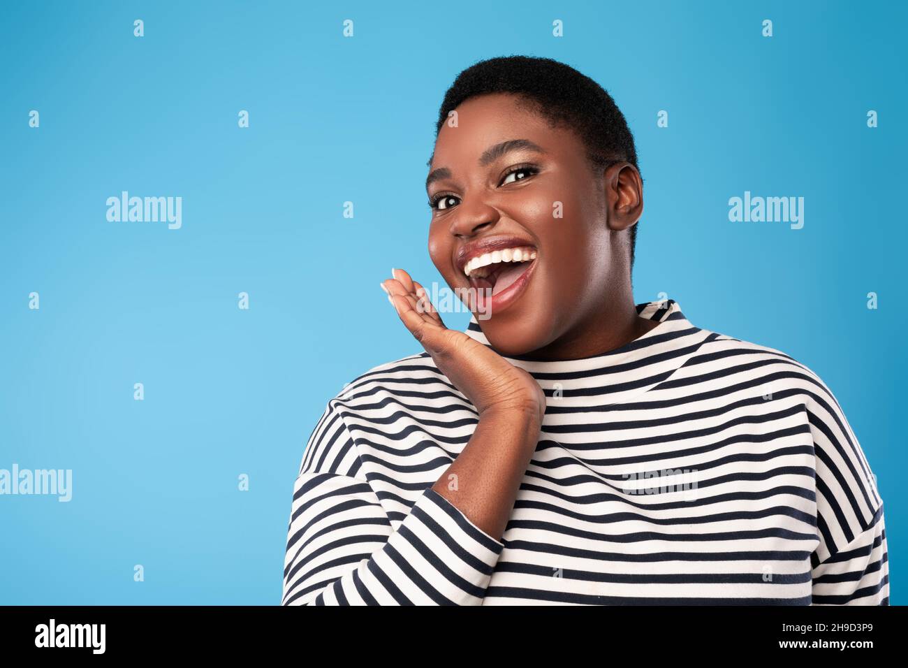 Donna africana urlando mano di tenuta vicino alla bocca giocosamente, sfondo blu Foto Stock