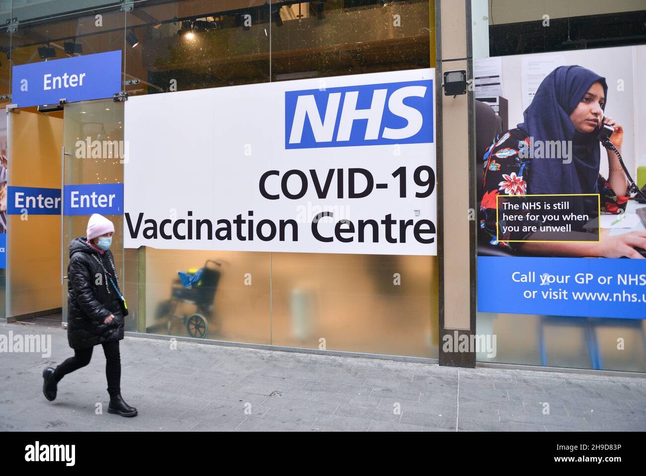 Una donna che passa accanto al centro di vaccinazione NHS Covid-19 a Westfield, Stratford. Il Regno Unito reintroduce le restrizioni pandemiche nell'emergere della variante Omicron COVID-19. I jab Booster saranno disponibili a gennaio. Foto Stock
