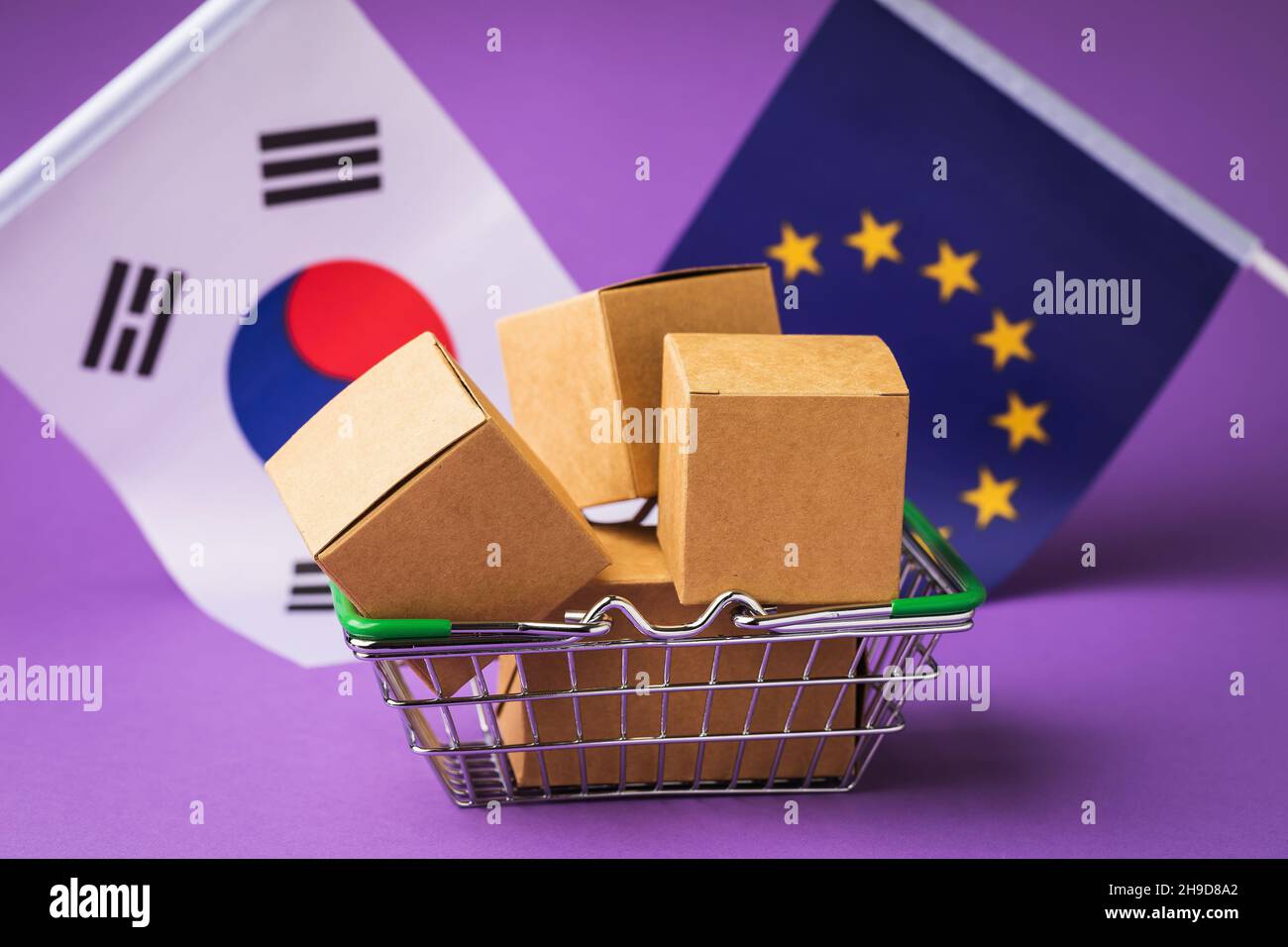 Scatole di cartone in un cestino alimentare, bandiere della Corea del Sud e dell'Unione europea su sfondo colorato, il concetto di commercio tra paesi Foto Stock