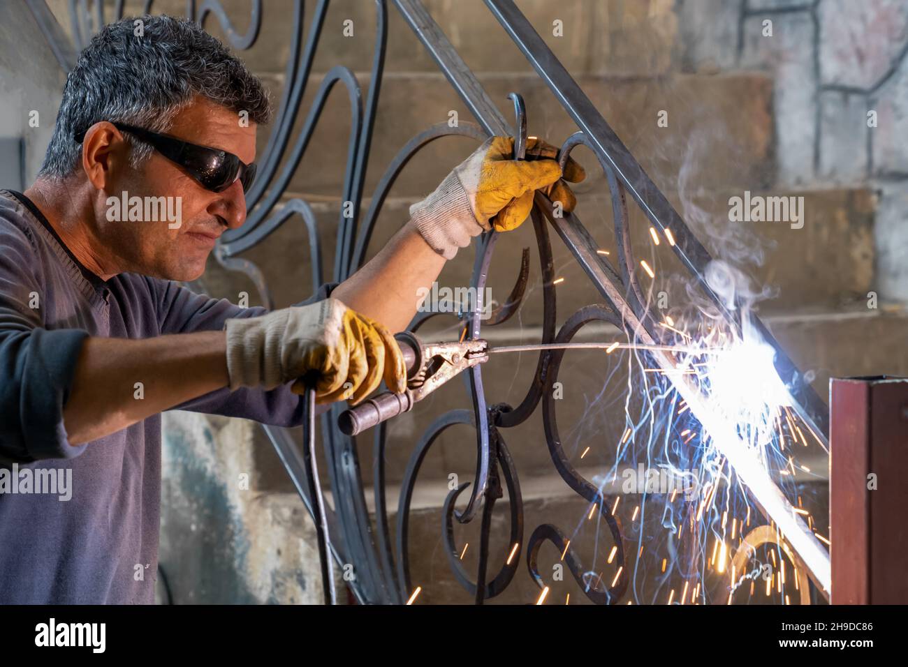 Uomo che indossa occhiali protettivi salda metallo con saldatrice. Le scintille provenienti dalla saldatura volano sui lati. Primo piano Foto Stock