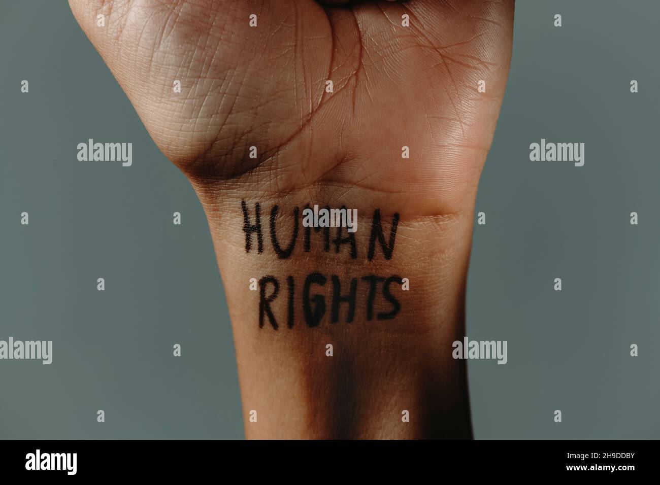primo piano del polso di un uomo con il testo diritti umani scritto in esso, su sfondo grigio Foto Stock