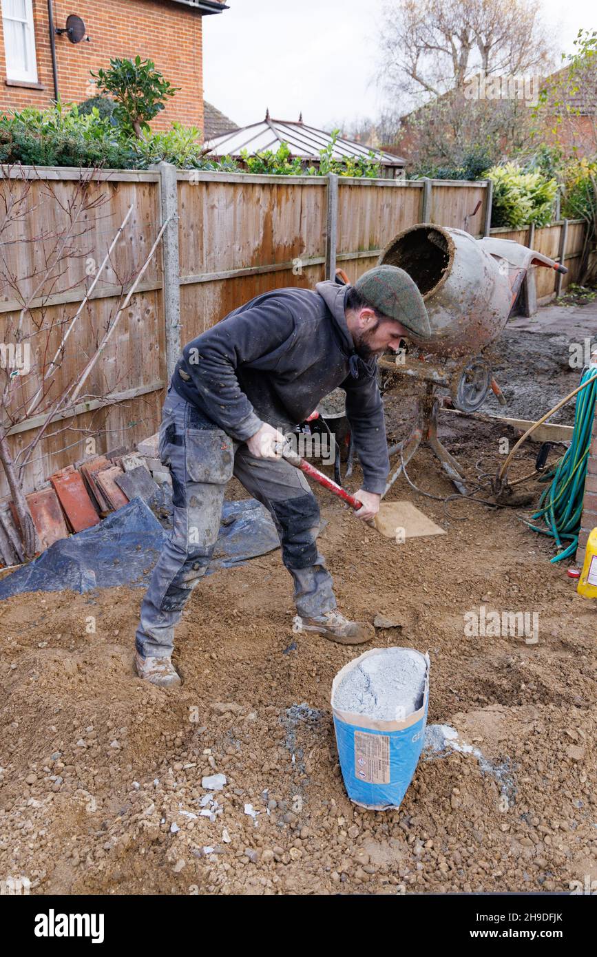 Un costruttore che fa cemento in un mescolatore di cemento, esempio di un operaio che fa lavoro manuale; lavoro di costruzione, su un cantiere, Inghilterra UK Foto Stock