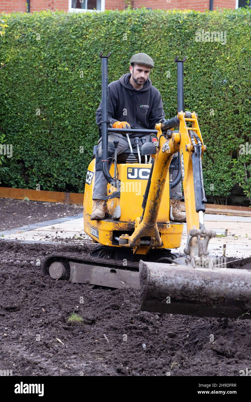 Lavoro specializzato UK; giardiniere di paesaggio UK - un uomo che opera un mini digger in un giardino domestico, Suffolk UK Foto Stock