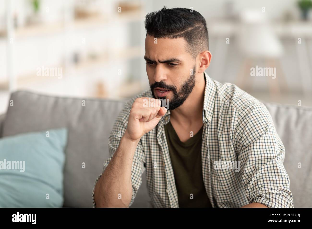 Coronavirus, influenza stagionale. Malato arabo tosse nel pugno, seduta sul divano, sensazione di malessere a casa, spazio libero Foto Stock