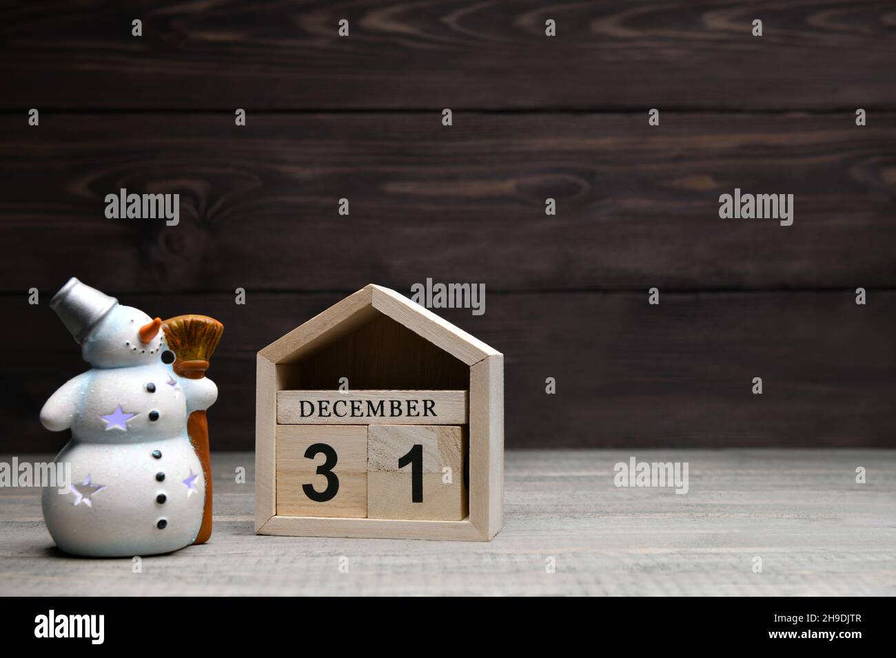 Decorazioni natalizie su sfondo ligneo: Cubetti di legno con i numeri dicembre 31 e un pupazzo di neve brillante. Messa a fuoco selettiva Foto Stock
