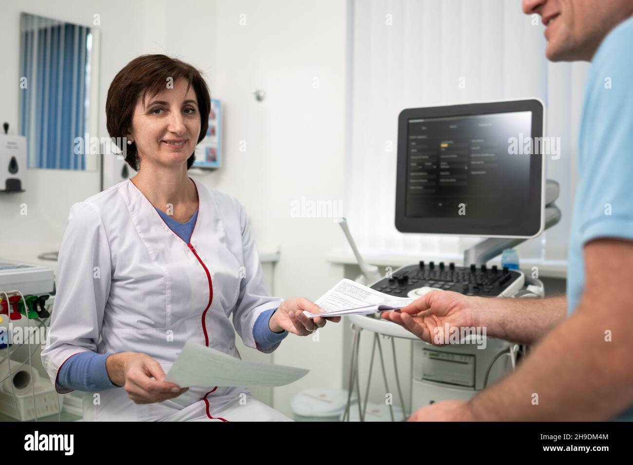 Il medico femminile consulta i risultati del test di tenuta del paziente maschile nelle mani in ufficio di clinica. Concetto di assistenza e cura del cuore. Esame medico. Donna terapista Foto Stock