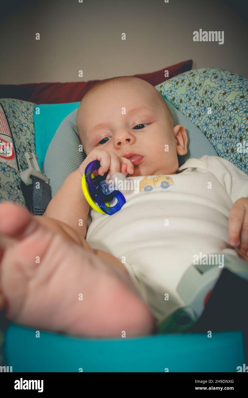 Il bambino di due mesi è sdraiato sul seggiolino per auto e tiene il succhietto in una piccola mano Foto Stock