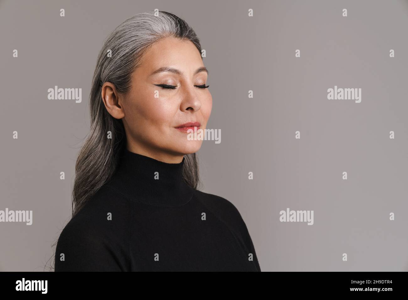 Donna bianca asiatica matura in posa con i suoi occhi chiusi isolato su sfondo grigio Foto Stock