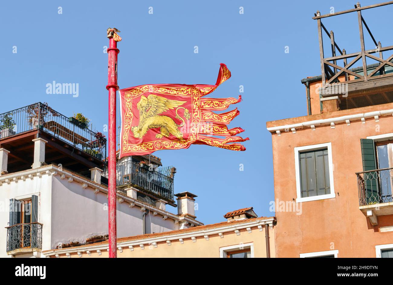 Bandiera di Venezia sullo sfondo della tradizionale architettura italiana, il principale simbolo veneziano il leone dorato alato di Marco evangelista Foto Stock