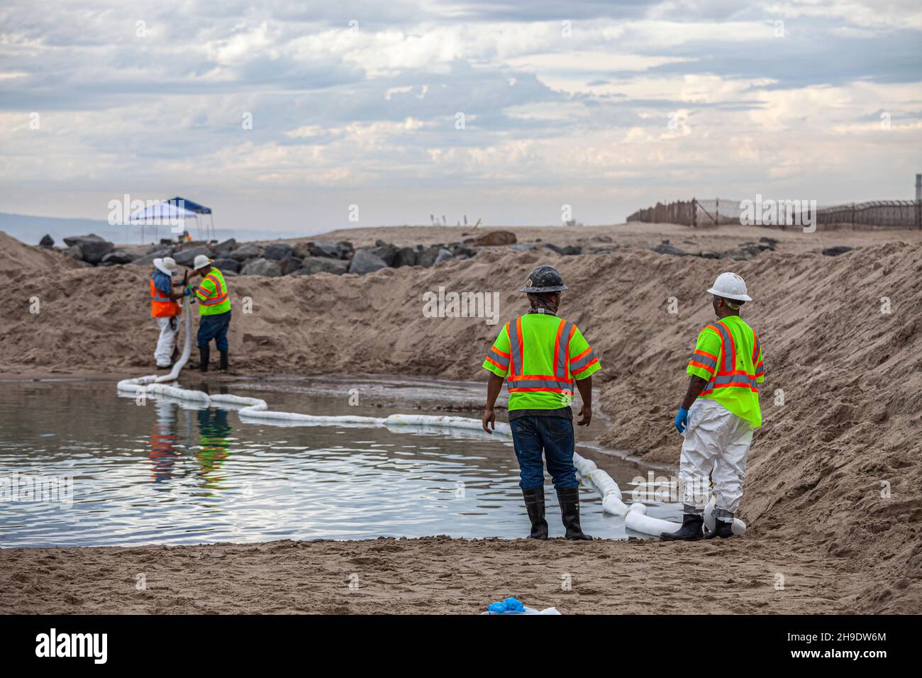 Un equipaggio di pulizia pulisce i lobi di petrolio e catrame e si affaccia su un ormeggio che è stato costruito per evitare che il petrolio si diffonda nel fiume Santa Ana che normalmente Foto Stock