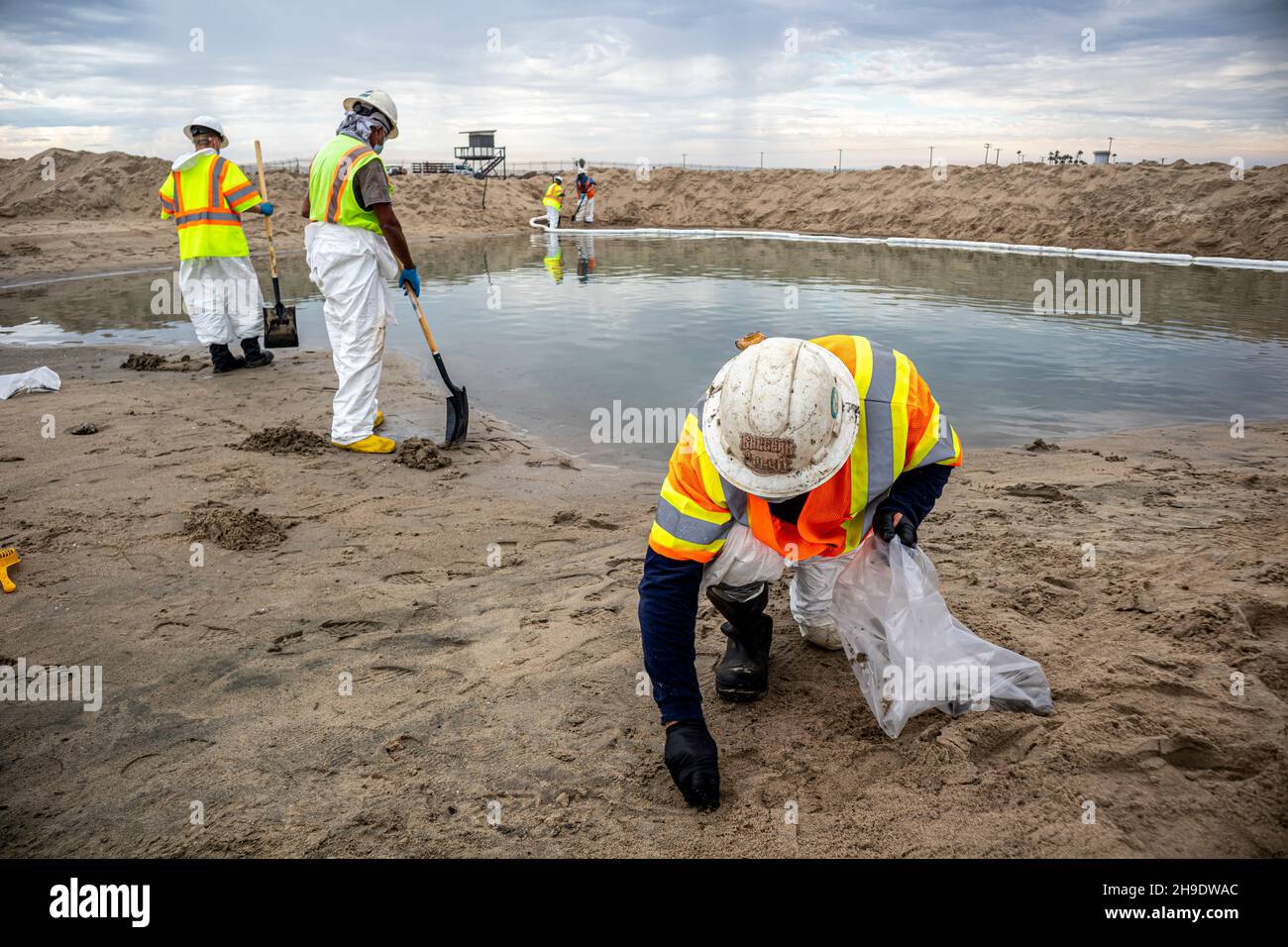 Un equipaggio di pulizia pulisce i lobi di petrolio e catrame e si affaccia su un ormeggio che è stato costruito per evitare che il petrolio si diffonda nel fiume Santa Ana che normalmente Foto Stock