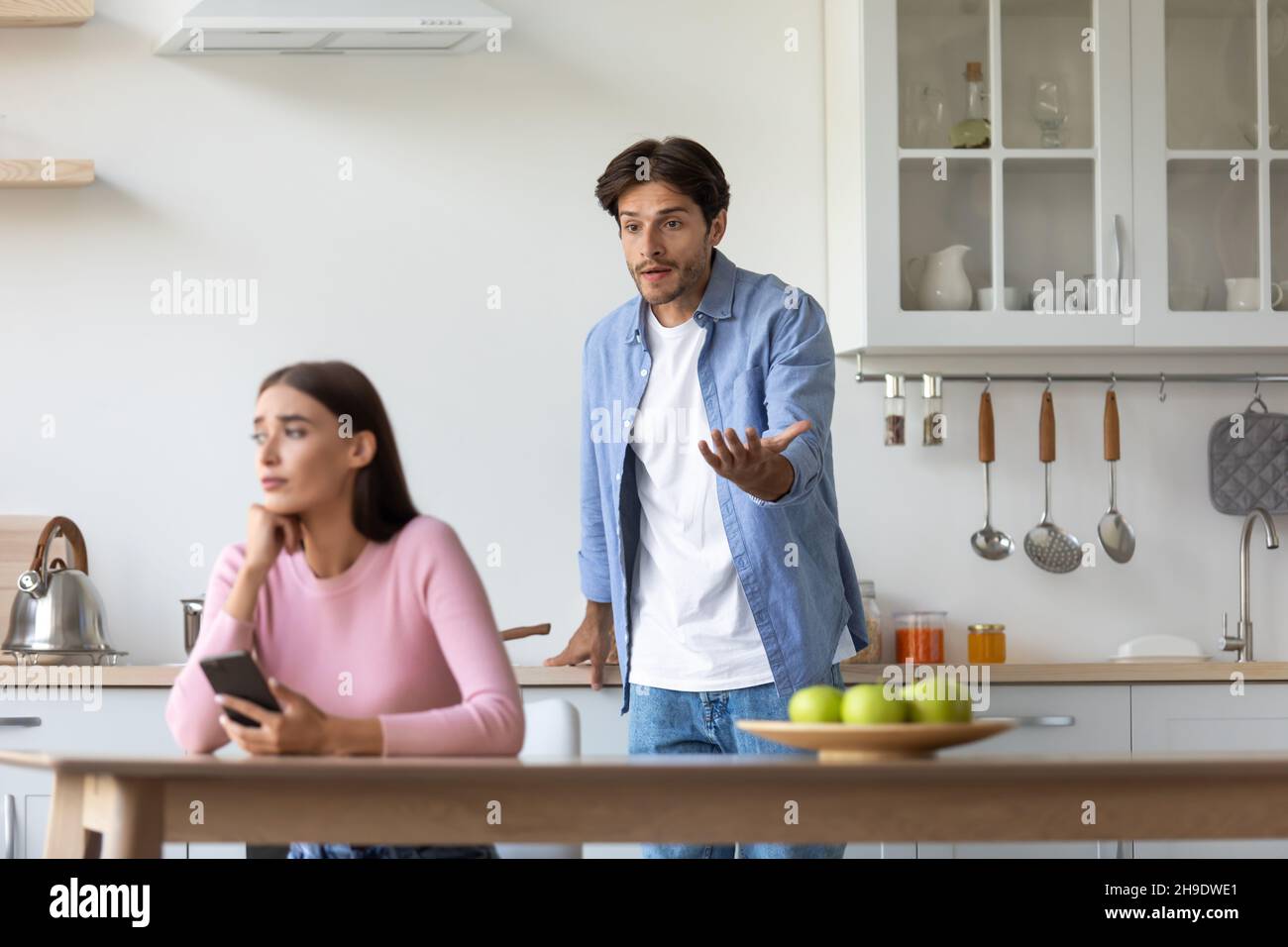 Triste millenaria donna europea con smartphone ignora offeso arrabbiato urlando marito in cucina Foto Stock