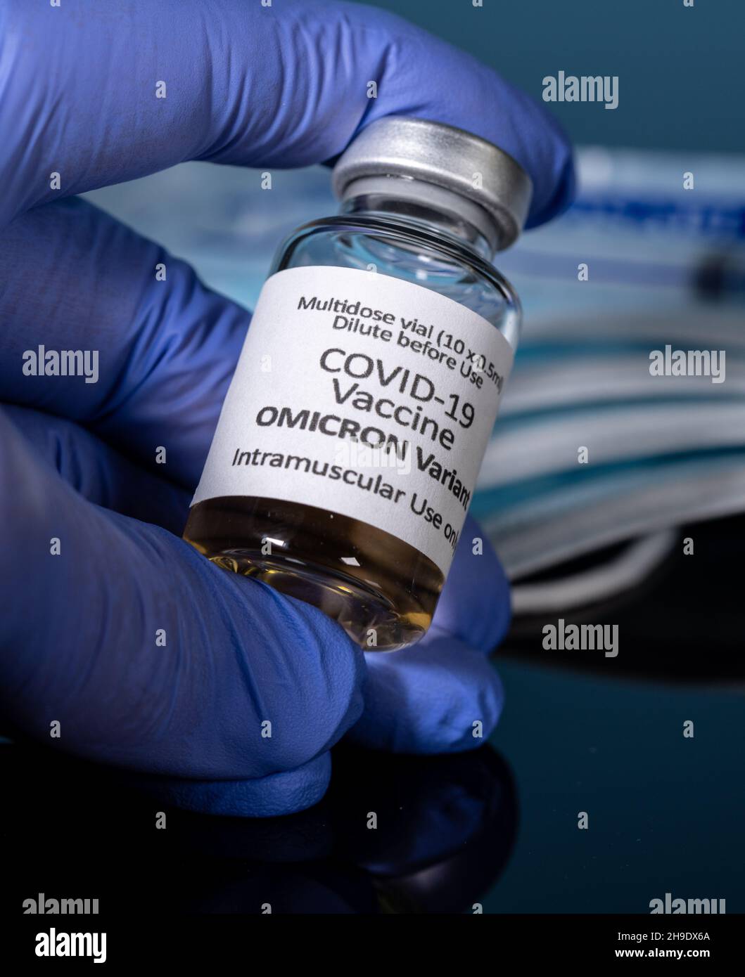 Vaccino per coronavirus Covid-19 sviluppato per la variante Omicron tenuta da una mano con guanti e mascherine per il viso sullo sfondo Foto Stock