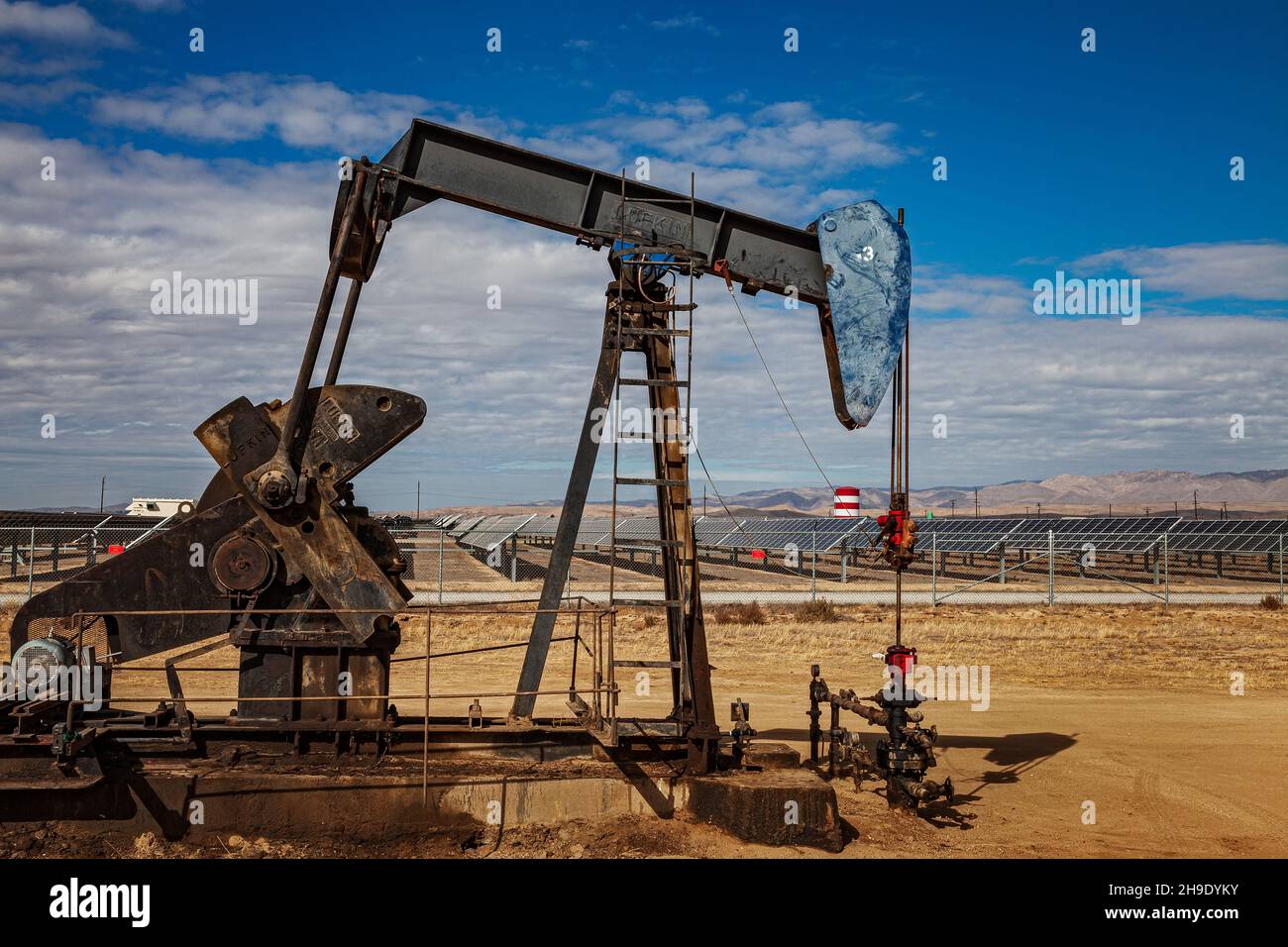 Pumpjack Lone situato nel mezzo di un grande impianto solare al di fuori di Bakersfield, Kern Coutny, California, Stati Uniti Foto Stock