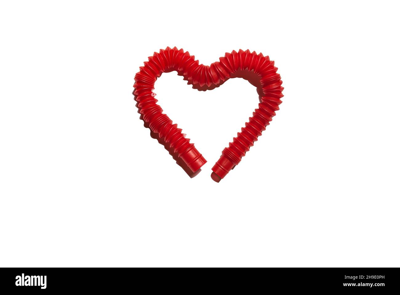 Steso rosso pop it tubo bambini giocattolo piegato a forma di cuore. Giocattolo antistress in plastica tagliato fuori con la sua ombra dura su sfondo bianco. Isolare Foto Stock