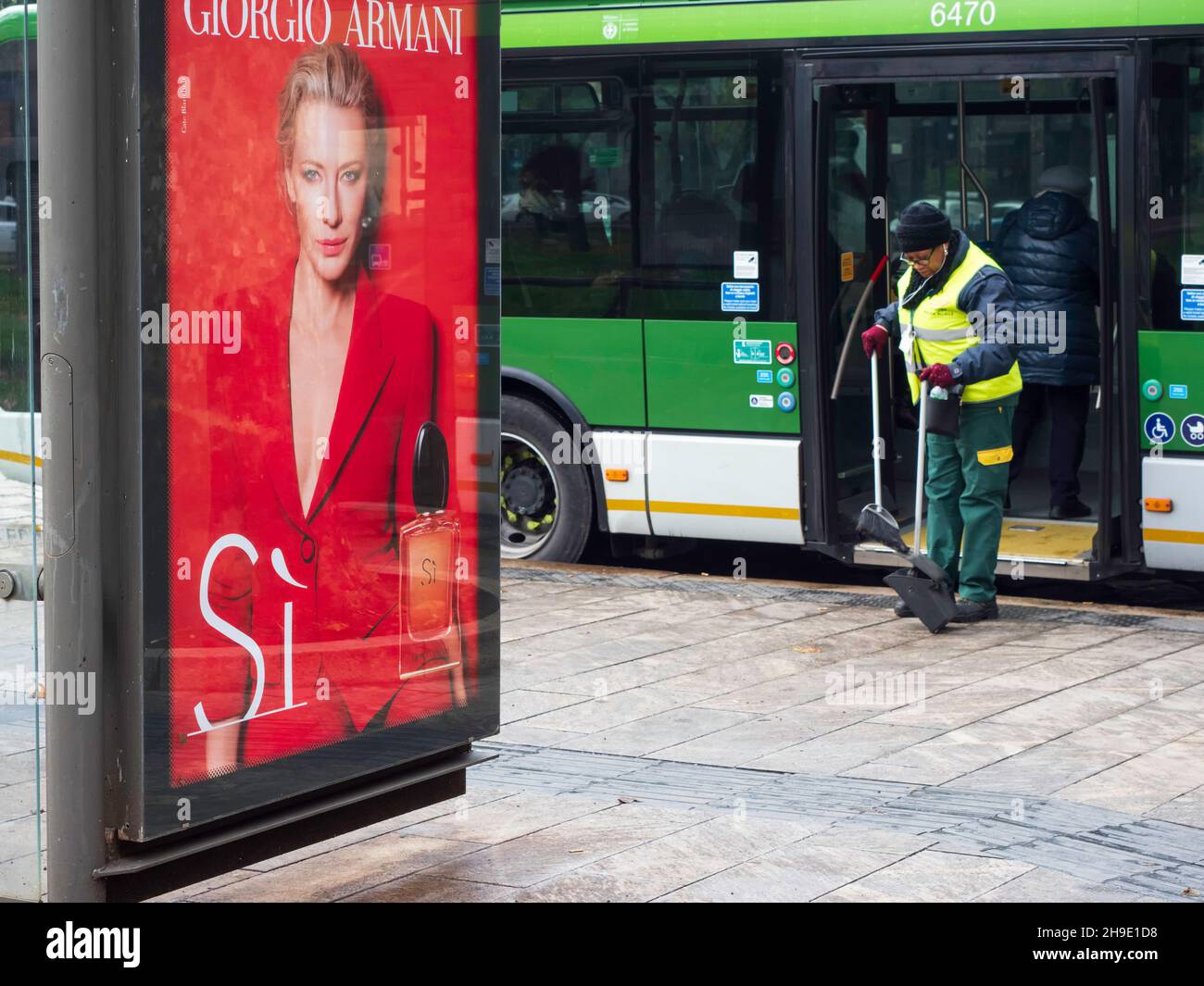 Milano, Lombardia, Italia. Dicembre 2019. Pulizia municipale che si affaccia sulla strada accanto a un poster pubblicitario per prodotti di lusso a Milano Foto Stock