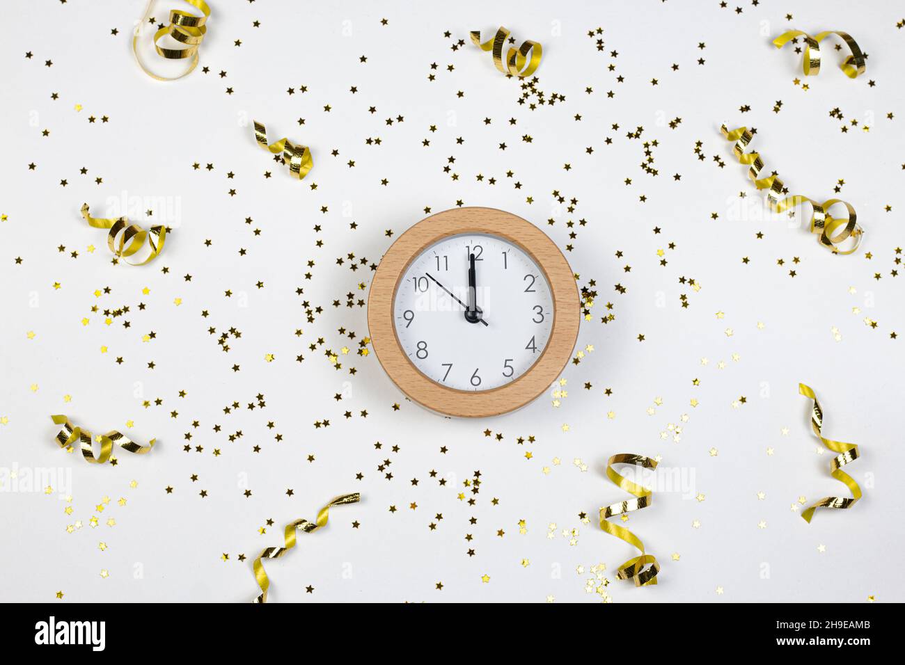 Concetto del tempo del partito. Orologio, stelle glitter e confetti dorati su sfondo bianco. Disposizione piatta. Foto Stock