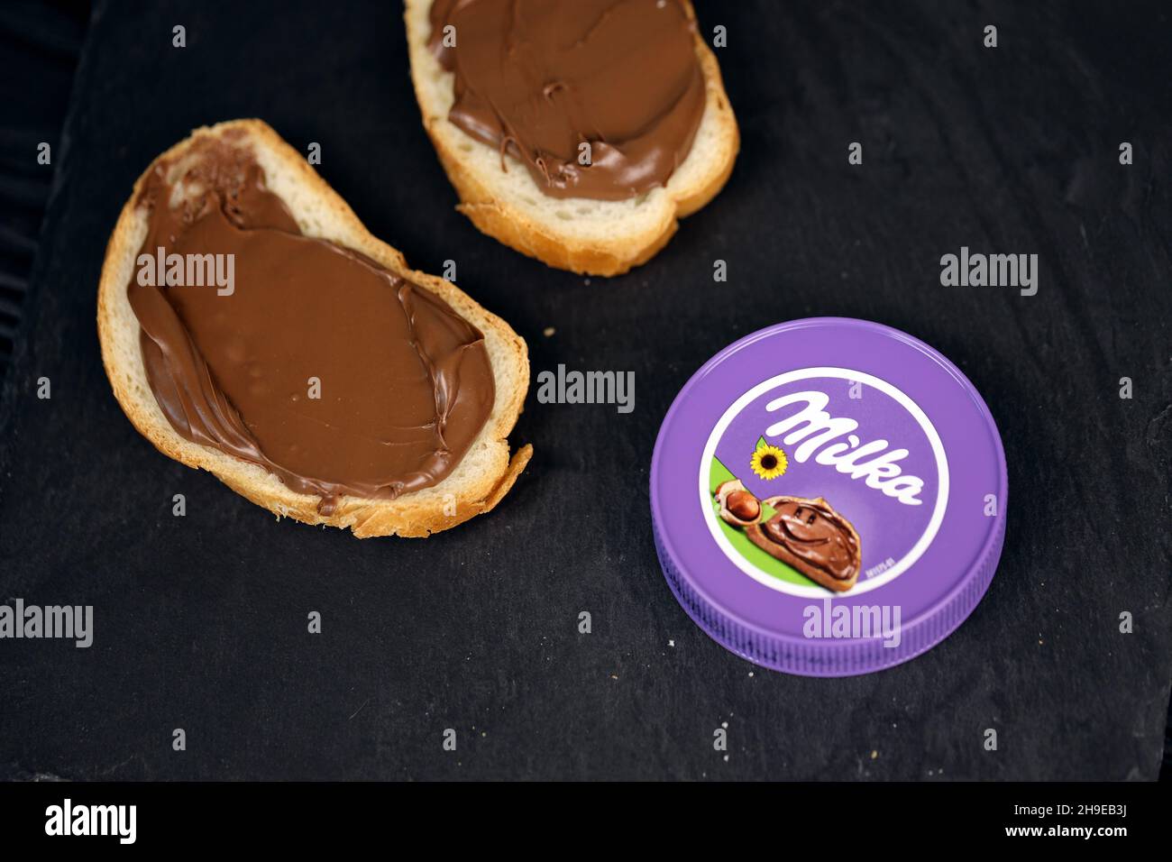 KHARKOV, UCRAINA - 2 LUGLIO 2021: Milka ha zuccherato il cacao della nocciola sparso con il disegno classico del colore lilla sul tavolo di legno nero Foto Stock