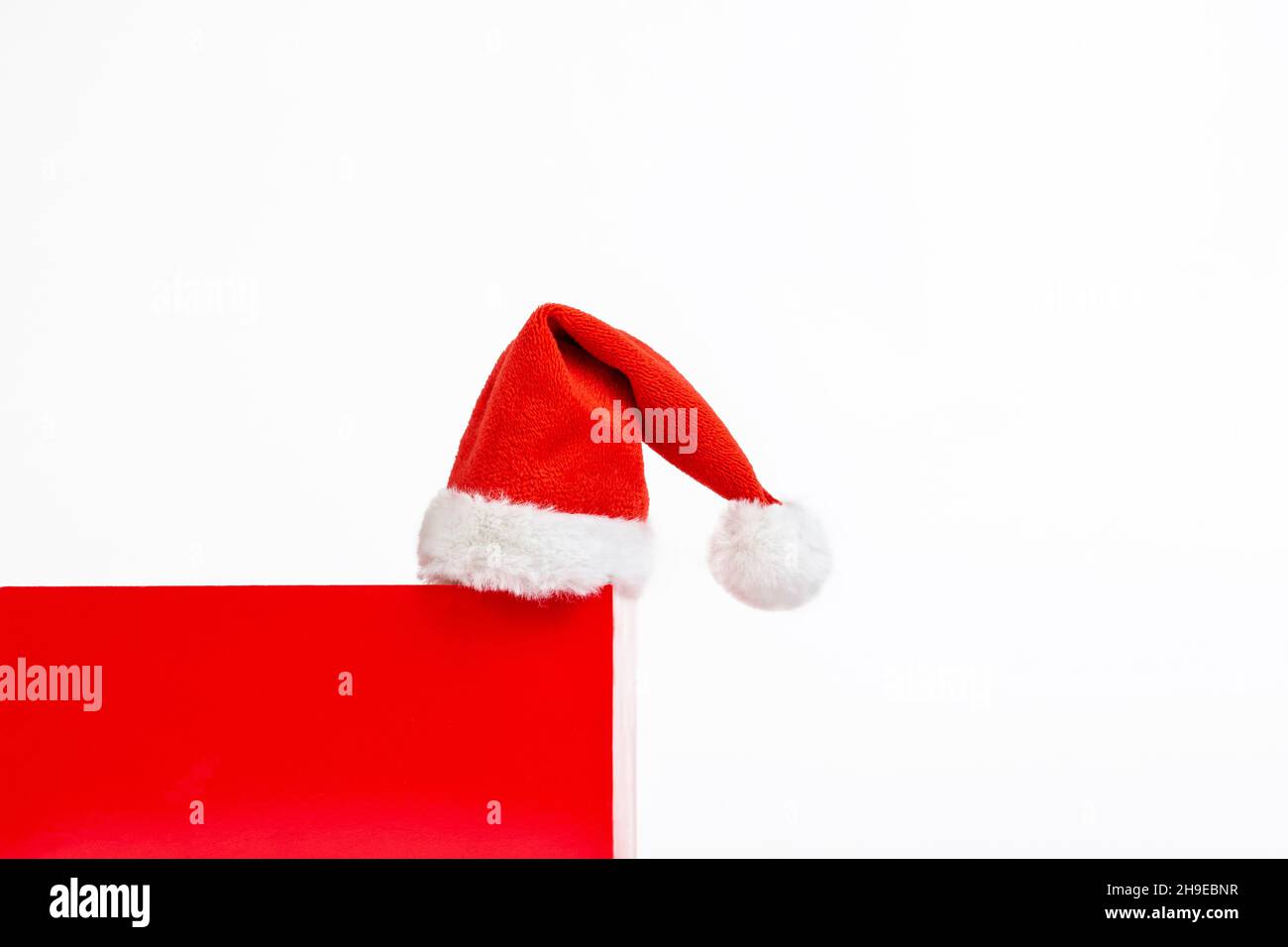 Composizione minima di Natale. Podio a forma di cubo rosso con cappello Babbo Natale su sfondo bianco con spazio copia. Foto Stock