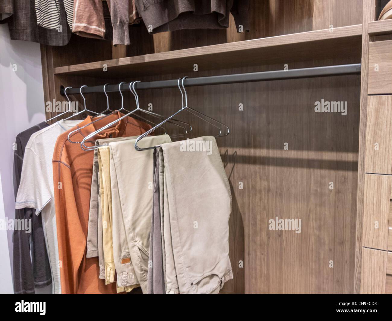 Un grande, passeggiata in armadio con camicie e pantaloni kaki appesi su appendiabiti Foto Stock