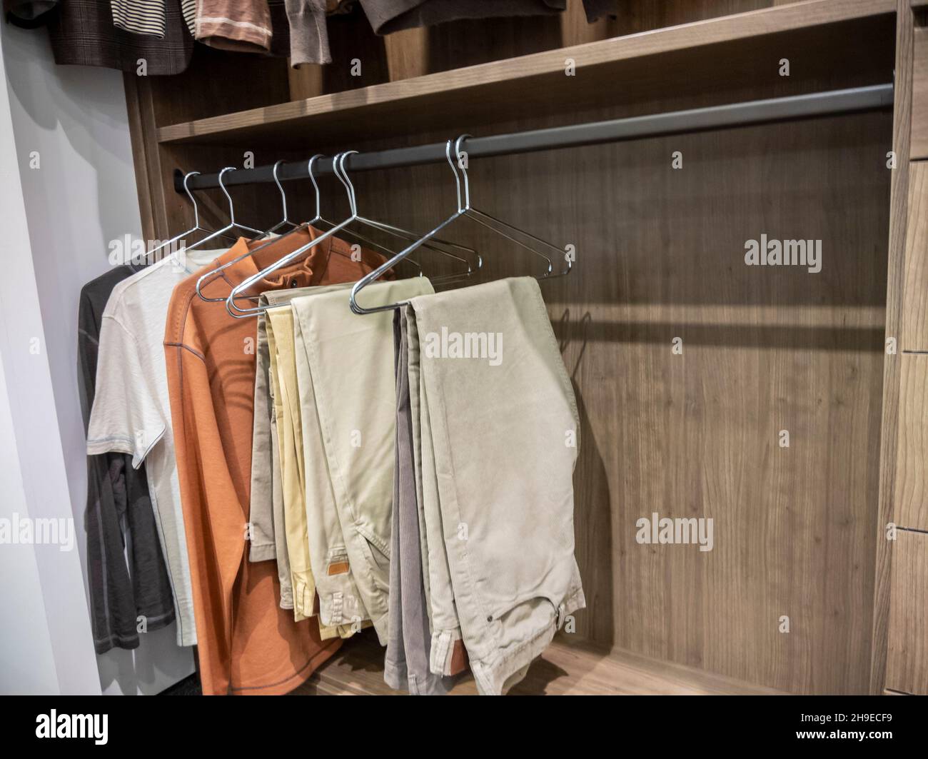 Un grande, passeggiata in armadio con camicie e pantaloni kaki appesi su appendiabiti Foto Stock