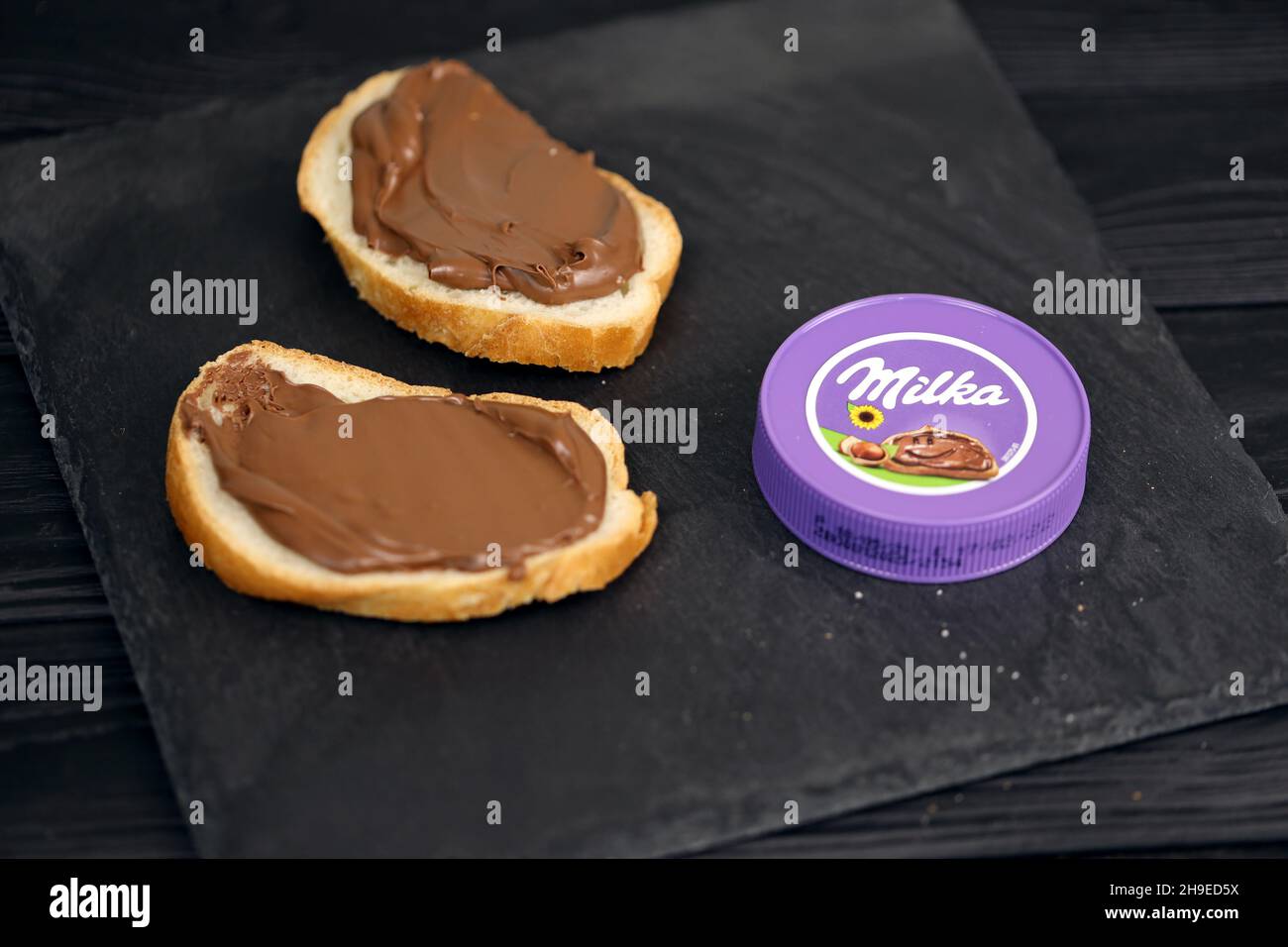 KHARKOV, UCRAINA - 2 LUGLIO 2021: Milka ha zuccherato il cacao della nocciola sparso con il disegno classico del colore lilla sul tavolo di legno nero Foto Stock