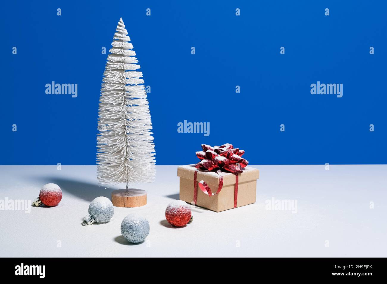 Bella banner di Natale o Capodanno con spazio per la copia. Albero di Natale giocattolo, scatola regalo con arco rosso e baubles di Natale su sfondo blu Foto Stock