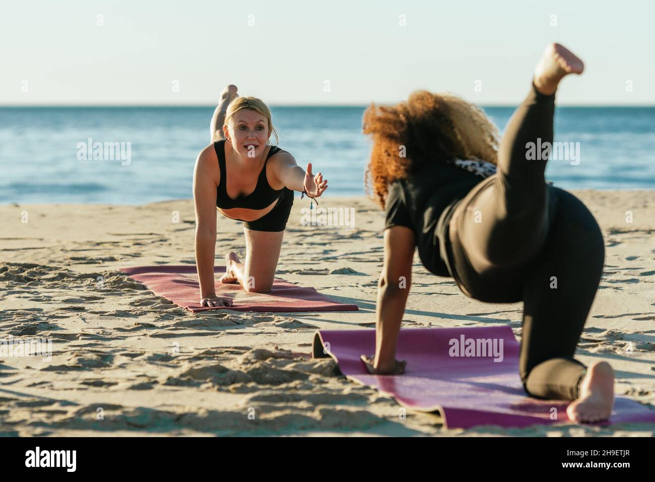 Allenatore di yoga che fa una lezione privata a una donna incinta sulla spiaggia Foto Stock
