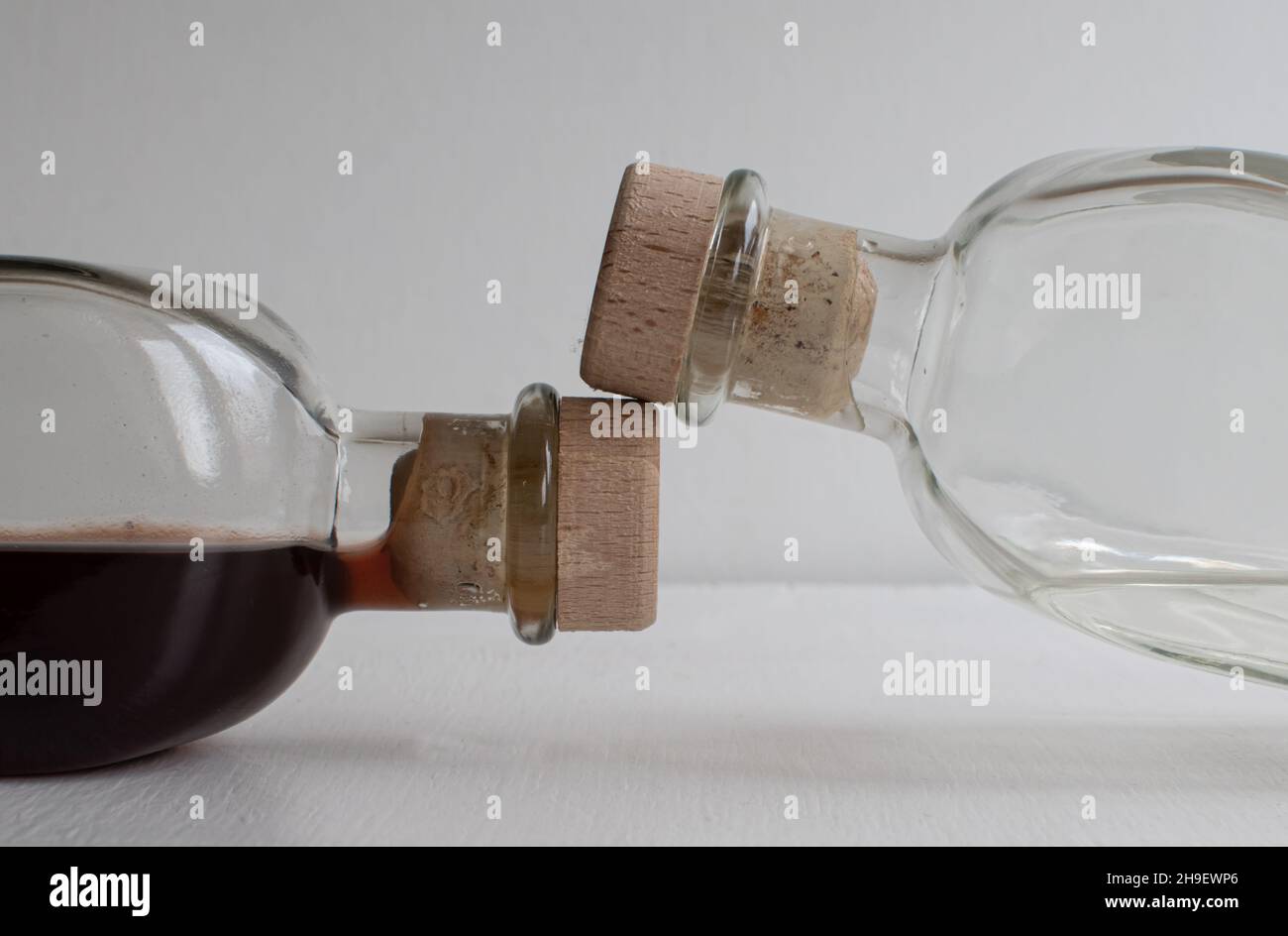 Due bottiglie di vetro con liquidi e tappi su sfondo sfocato chiaro Foto Stock