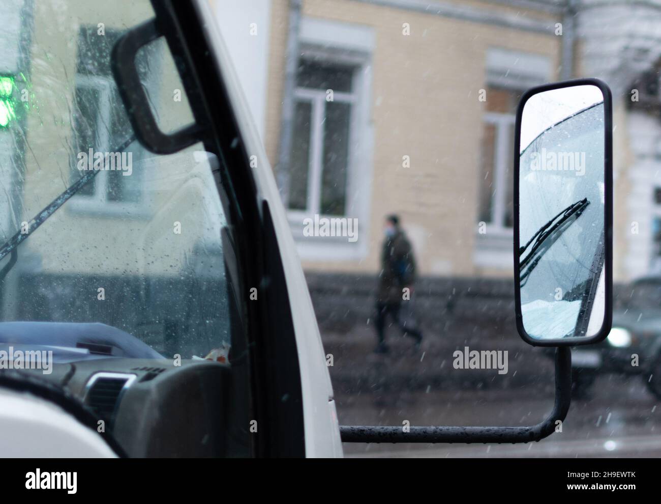 Specchio laterale del camion sullo sfondo sfocato della strada della città in cattive condizioni meteorologiche Foto Stock