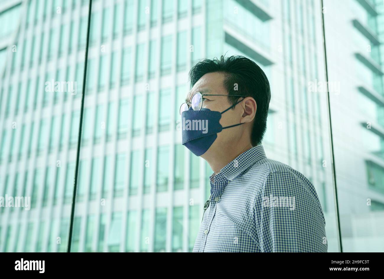 Uomo d'affari asiatico indossare maschera con ufficio edificio sullo sfondo. Business durante il concetto di pandemia di Covid-19. Spazio di copia. Foto Stock