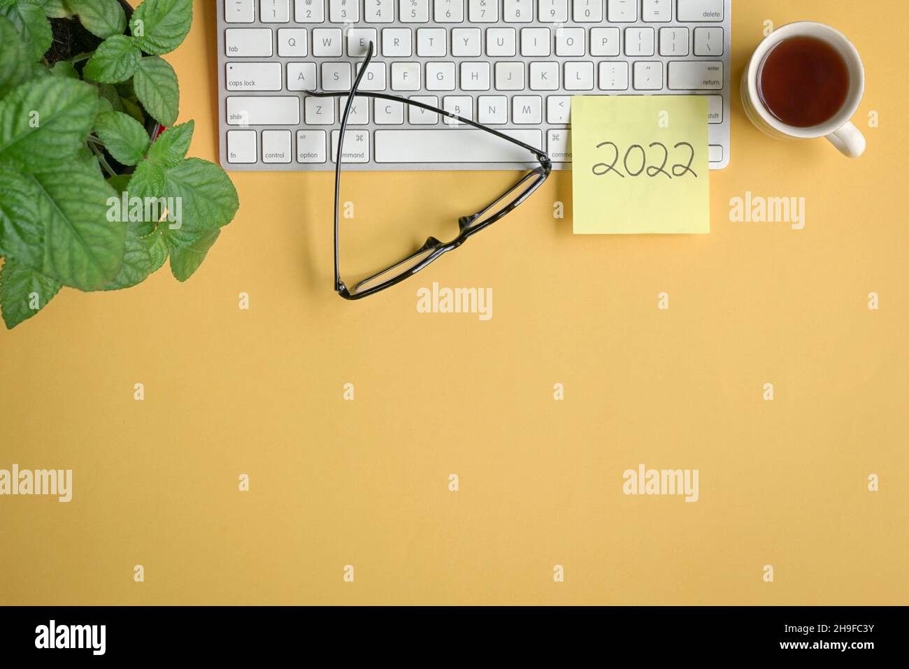 2022 scritto su bastone di carta giallo sulla tastiera con caffè, occhiali e pianta. Disposizione piatta, spazio di copia. Foto Stock