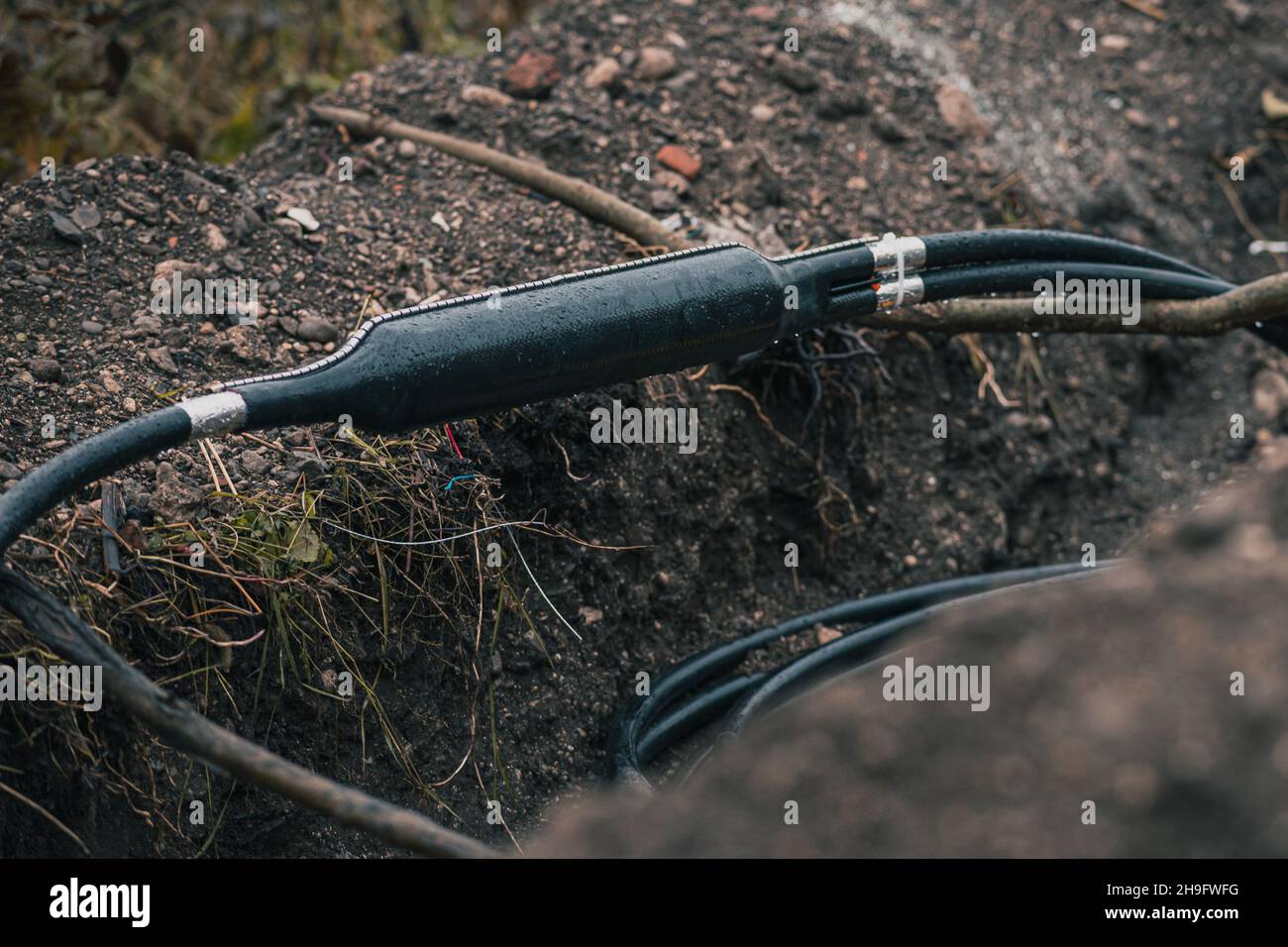Collegamento di cavi ottici industriali, suddivisione a Y di un cavo, schermato in un contenitore in plastica visto scavato da terra o trincea in un cantiere. Foto Stock