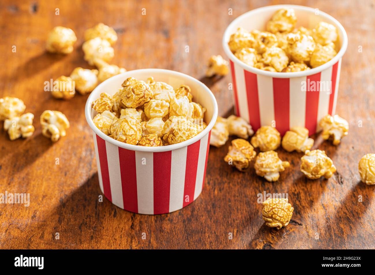 Popcorn caramello dolce in tazza di carta su tavola di legno. Foto Stock
