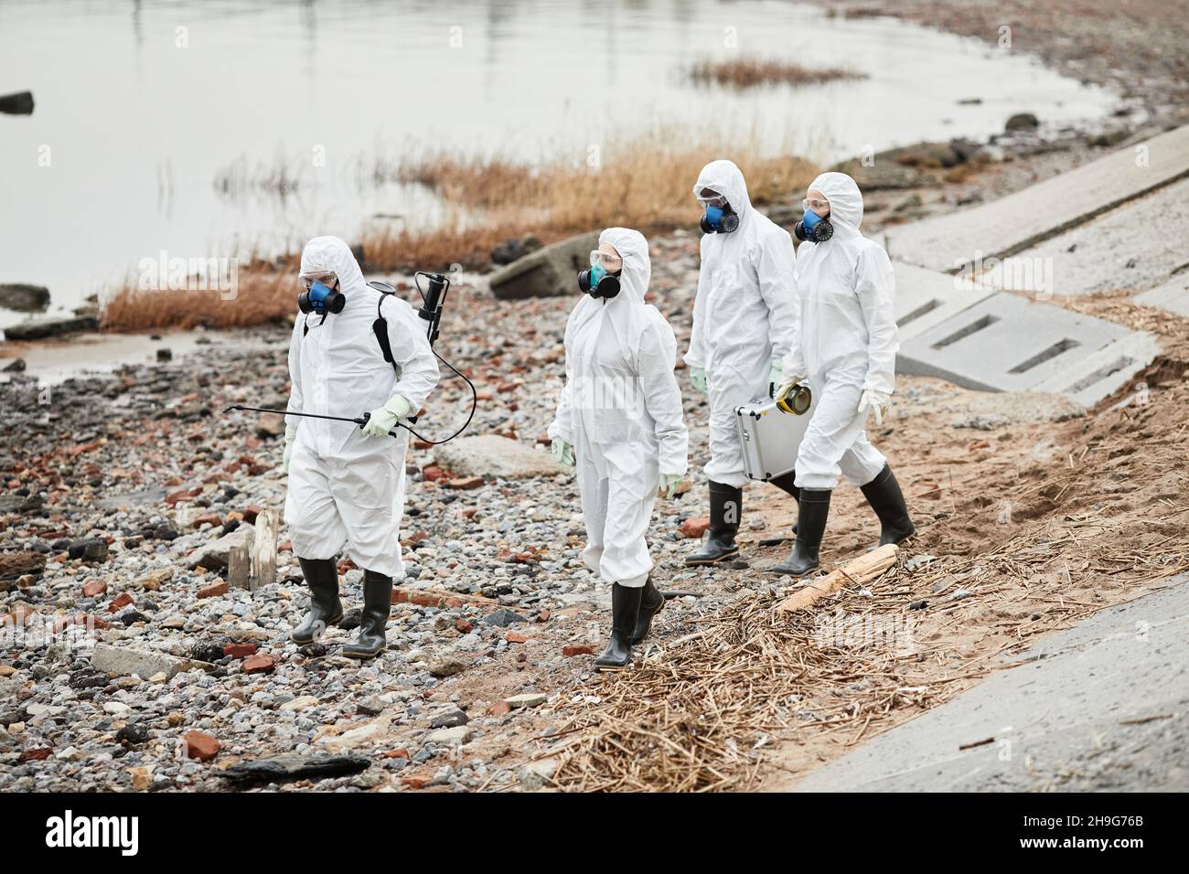 Gruppo di lavoratori che indossano tute nocciole che camminano in acqua all'aperto, concetto di rifiuti tossici, spazio di copia Foto Stock
