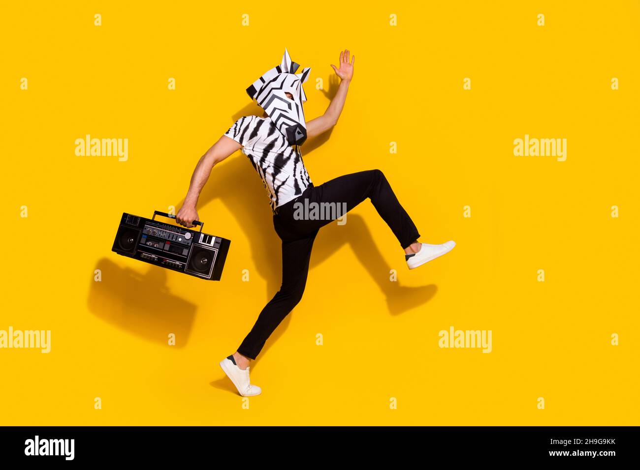 Foto lato profilo a tutta lunghezza di ragazzo bizzarro in zebra maschera di tenuta boom box punto discoteca isolato su sfondo di colore giallo lucido Foto Stock