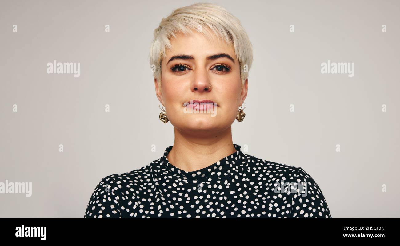 Ritratto di una donna bionda in piedi da sola in uno studio. Primo piano di una donna alla moda di metà adulto che guarda la fotocamera con sicurezza mentre si alza di nuovo Foto Stock