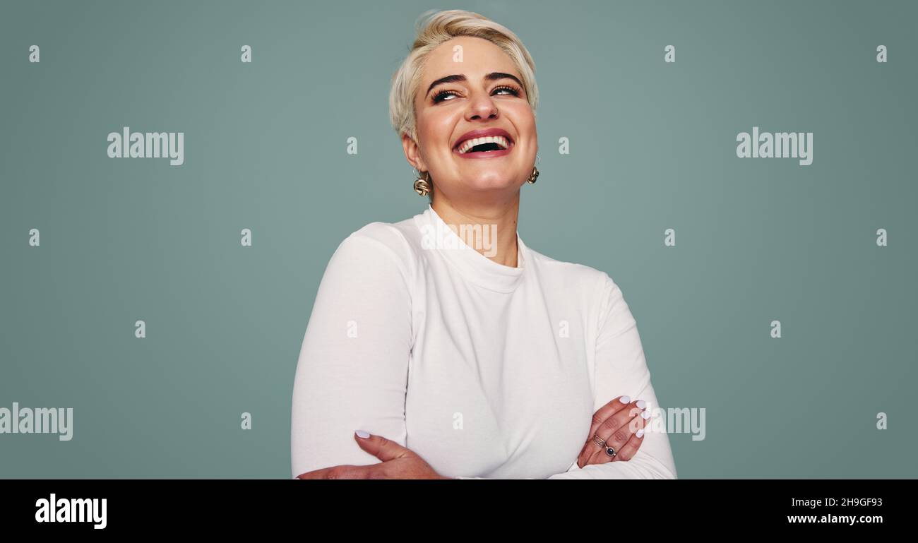 Bella donna bionda ridendo in uno studio. Felice donna di metà-adulto che guarda via allegro mentre in piedi contro uno sfondo studio. Moda Foto Stock