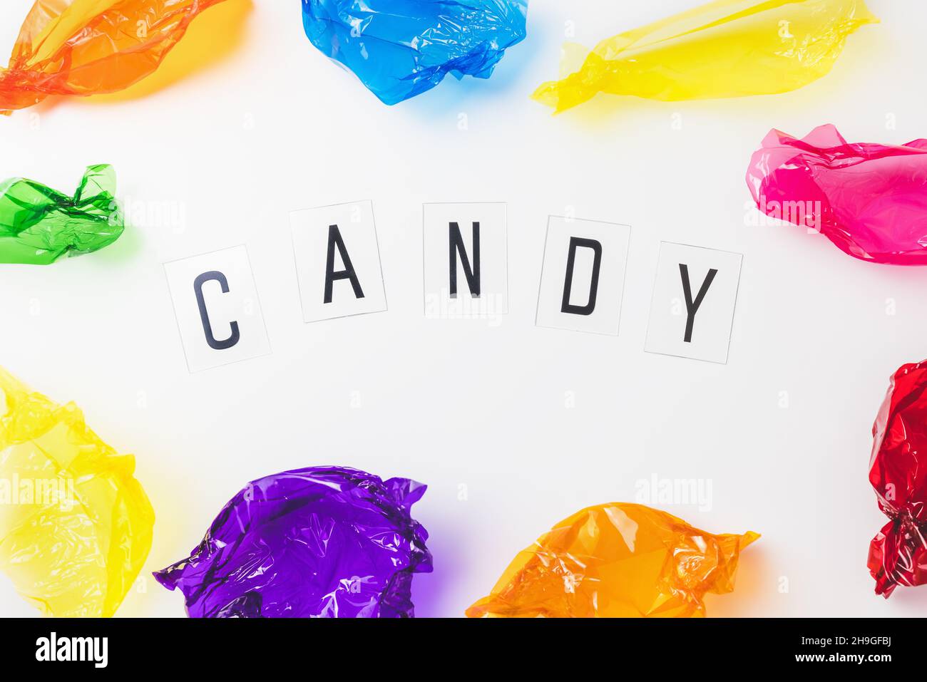 Coloratissimi involucri di caramelle e testo CARAMELLE su bianco. Concetto di dolci allo zucchero. Sfondo colorato astratto Foto Stock
