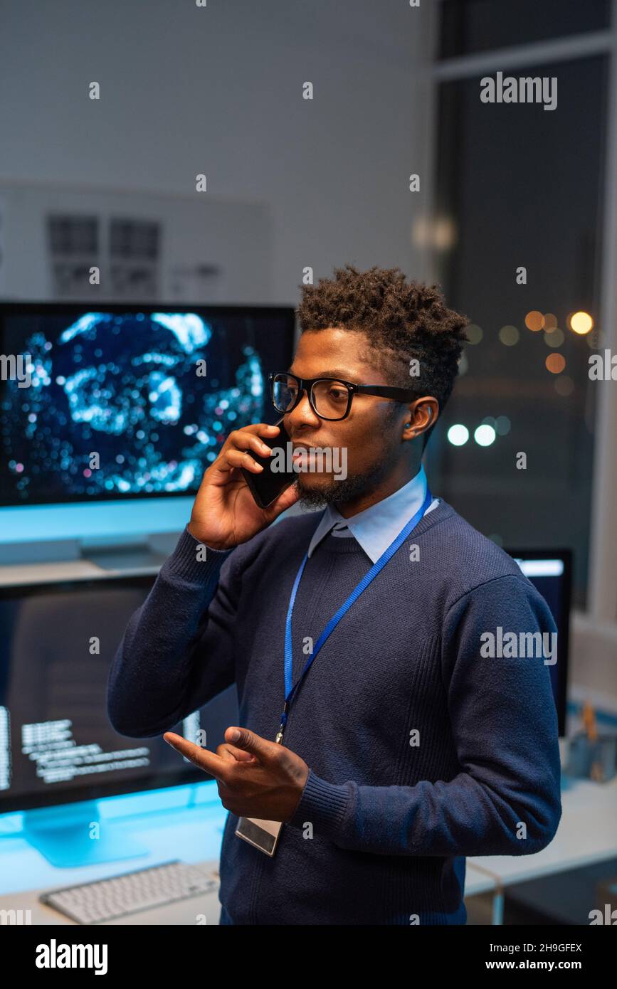 Giovane programmatore ben vestito che comunica su smartphone con uno dei clienti della società di servizi di sicurezza informatica Foto Stock