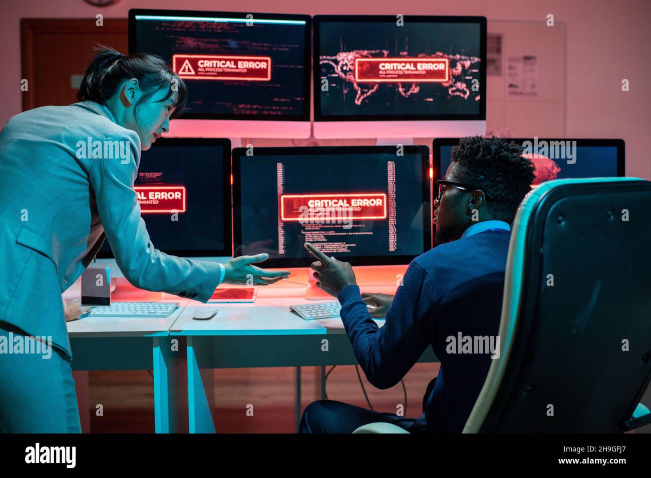 Due giovani programmatori interculturali che cercano di risolvere il problema dell'accesso ai dati interagendo di fronte ai computer Foto Stock